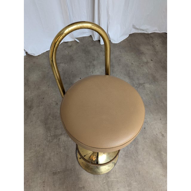 Vintage elegant bar stool is made from brass base and backrest and leather like seat. The chair was made in the 1970s in...