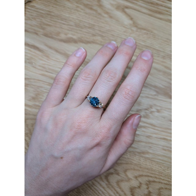 Crafted in solid 14K gold, this exquisite three-stone ring showcases a brilliant 2.1-carat Swiss Blue Topaz, flanked by...