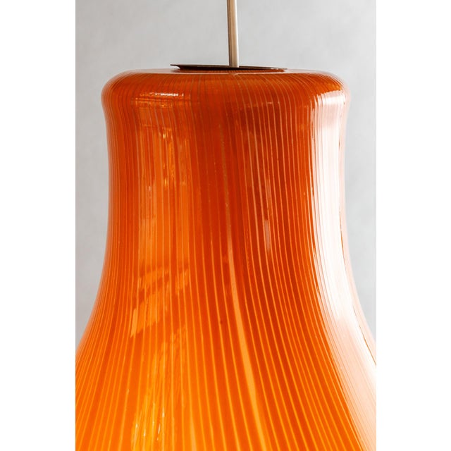 Pendant lamp from the Anemone series with an elongated (bulb-shaped) diffuser in translucent glass with orange rods....