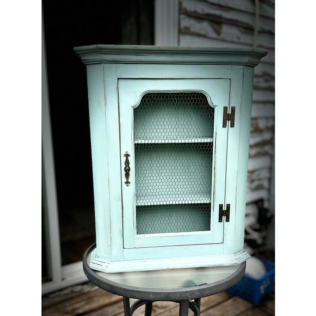vintage wooden cabinet, upcycled with a light sage green or duck-egg blue paint finish. It features a single door with a...