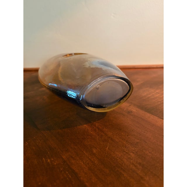 A striking hand-blown art glass vase featuring a sculptural oval form with a distinctive pierced center opening. The glass...