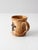 A vintage studio pottery mug featuring a raised fleur-de-lis motif on one side. The glaze blends golden brown and cream...