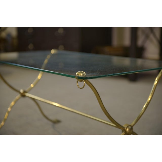 An elegant coffee table with a neoclassical feel, combining a rectangular glass top and a gold-tone metal base. The...