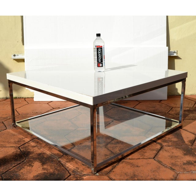 Modern White Glossy Lacquered Top Chrome Coffee Table with Tempered Glass Bottom Shelf. Features a square polished chrome...