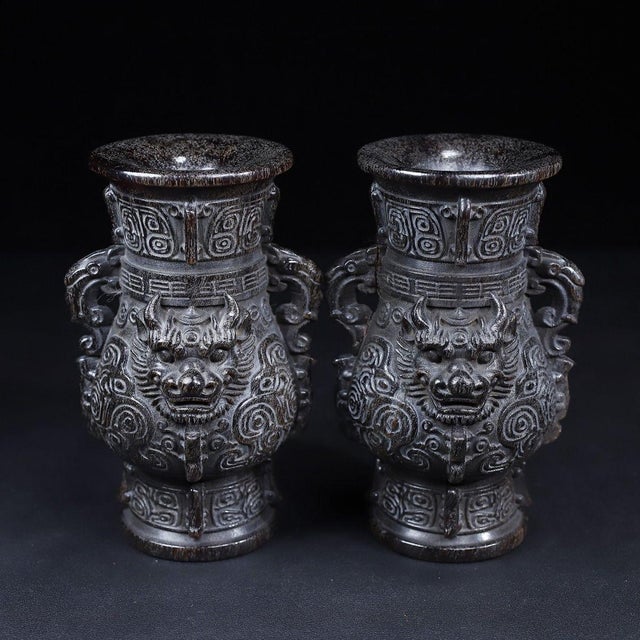 This is a striking pair of matching decorative vases, expertly carved to resemble dark horn or hardwood. The vases feature...