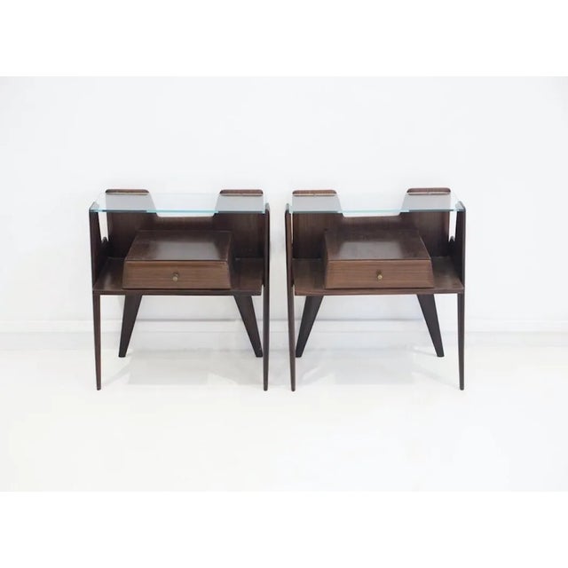Pair of 1950s Italian side tables or nightstands with one drawer. Made of dark wood with glass top and brass details.