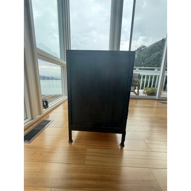 A striking industrial-style cabinet with a hand-riveted iron frame, glass front doors, and glass side panels that let...
