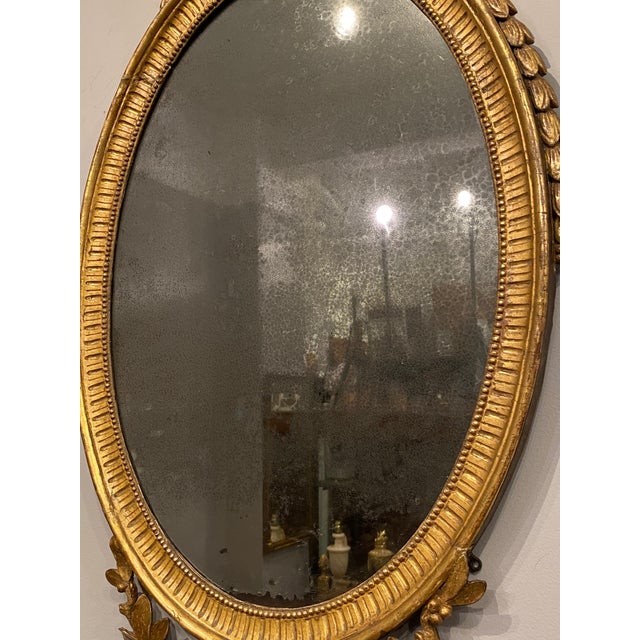 A George III oval giltwood mirror, late 18th century The urn shaped finial centered on foliate swags the oval frame with...