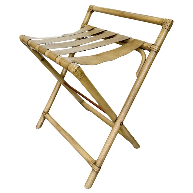 A mid-century folding luggage rack featuring a sturdy bent rattan frame paired with thick, supple tan vinyl / faux leather...