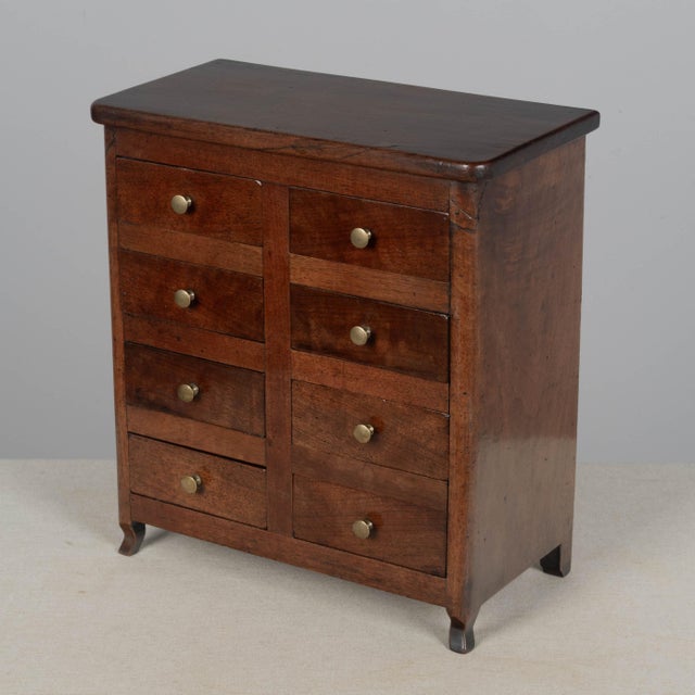 A 19th century French Country miniature chest hand-crafted of solid walnut with eight small dovetailed drawers with brass...