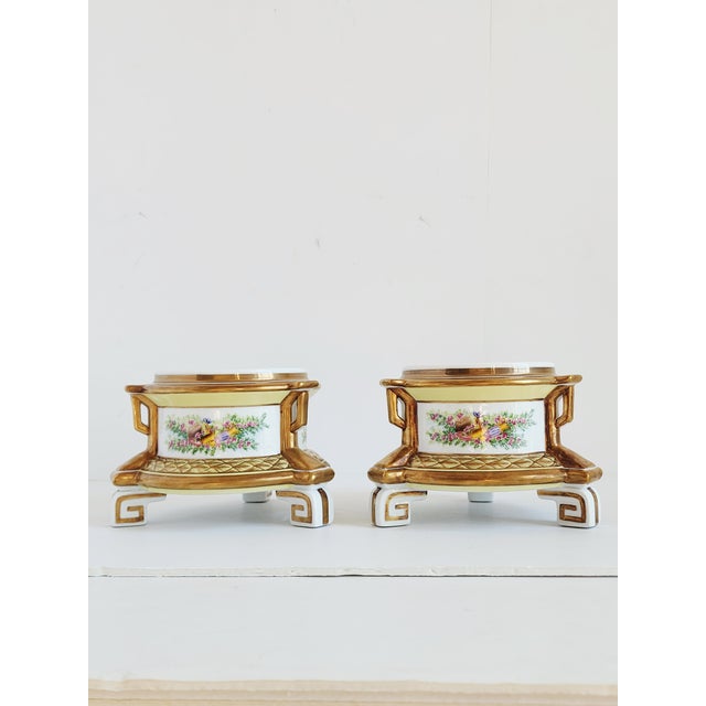 Pair of Chelsea House French style porcelain cachepots, featuring handpainted floral panels and Greek key motifs tripod...