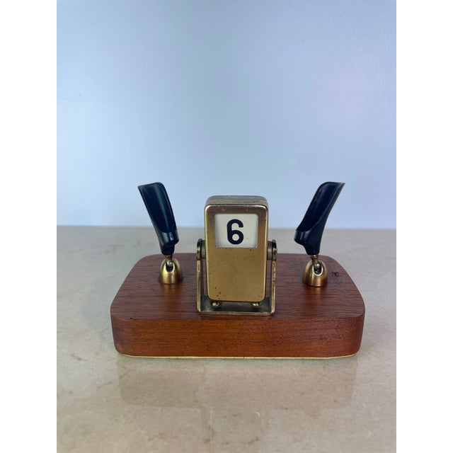 Charming vintage desk accessory combining a mechanical flip calendar with dual pen holders, mounted on a solid walnut...