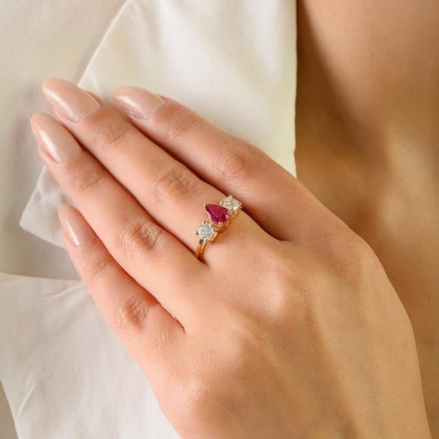 This elegant three-stone ring features 1 pear cut ruby totaling 0.57 carats, set in 14K yellow gold. the ruby measure...