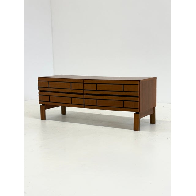A sleek, low Italian sideboard crafted from wood, with a bold, minimalist design. The drawers feature refined black lines...