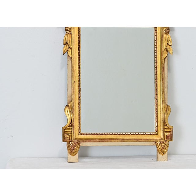 A French petite mirror in the Louis XVI style, dating to the 19th century, with gleaming carved giltwood crown. At the top...