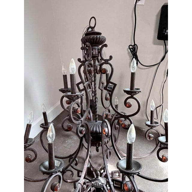A dramatic large two-tier wrought iron chandelier with 12 candle-style light positions, ornate scrollwork throughout, and...