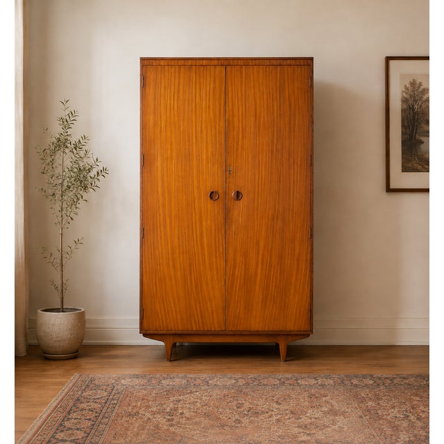 A stylish 1960s Uniflex wardrobe in beautifully figured teak veneer, featuring recessed circular handles and tapered legs....