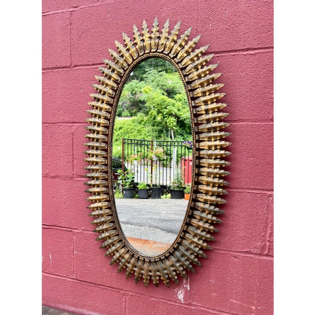 This lovely Spanish mid-century oval gilt metal sunburst mirror features small pointed rays surrounding a sturdy interior...