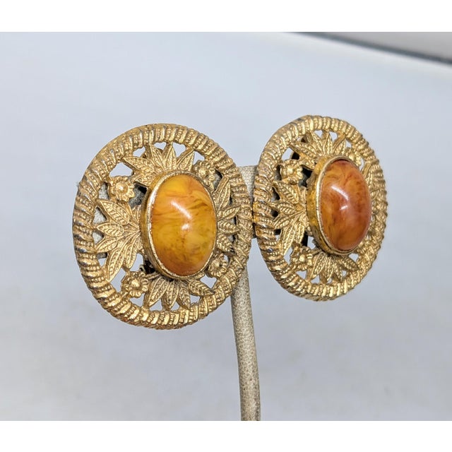 1980s goldtone round cabochon faux-orange swirl agate rhinestone with flowers and leaves cut out surround clip earrings....