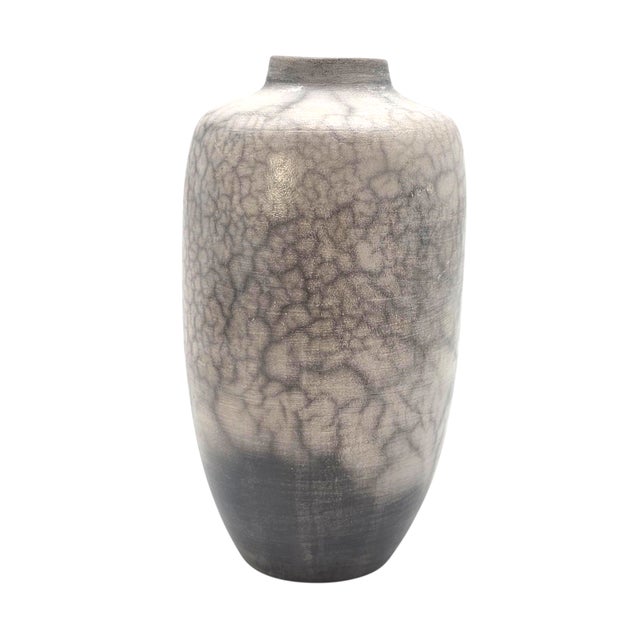 This vessel carries the quiet breath of fire and smoke, its pale surface marked with darkened veins that wander like...