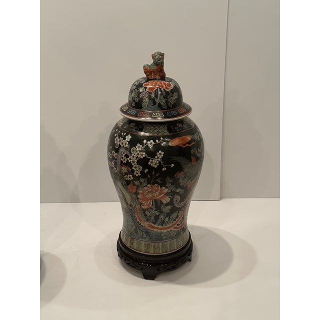 Impressively large intricately painted porcelain lidded urns having striking black background and decorated with cranes,...