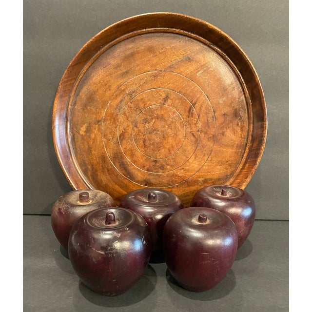 A set of five carved folk art apples in a dark wood, each unmarked with varying patinas and shapes. All on a round carved...