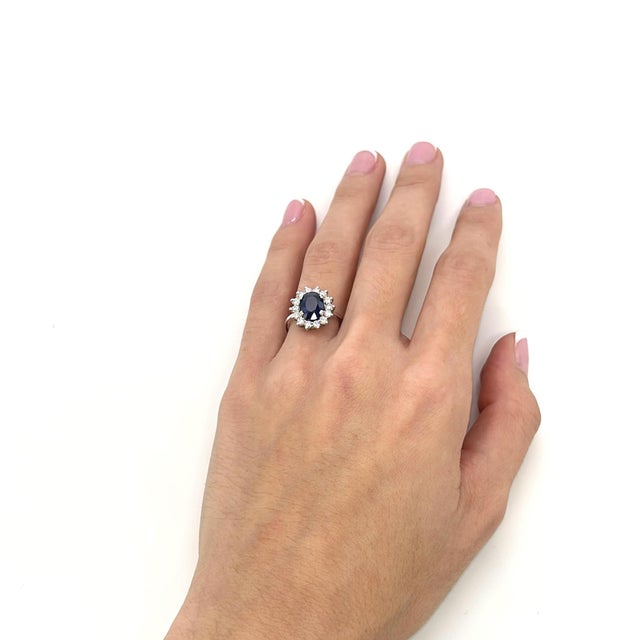 Her is a 14k White Gold Princess Diana Inspired Ring with a 14 Diamond Halo Surrounding the 2.2ct Oval Blue Sapphire...
