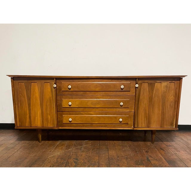 Mid-Century Modern credenza or dresser with dual side cabinets with sculpted doors, three dovetail drawers with pulls...