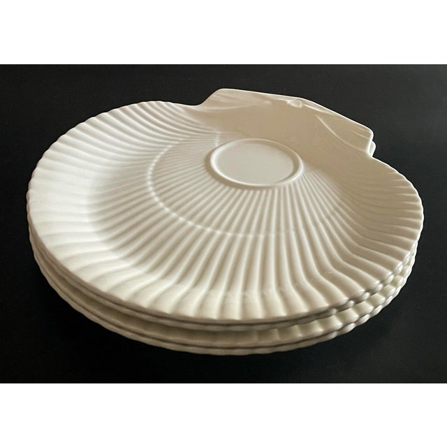 A set of four shaped plates in a cream white with scallop shell fluting made by Wedgwood.