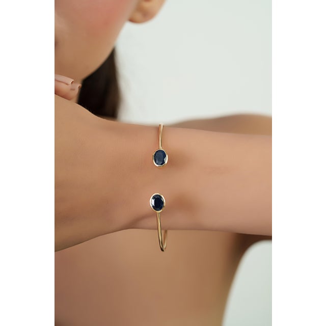 This open cuff bangle bracelet features 3.08 carats of natural blue sapphires set in 14K yellow gold. Each sapphire...