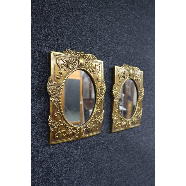 Pair of decorative Syroco wall mirrors featuring ornate molded floral and foliate relief with a warm gilt finish. Each...