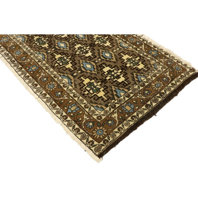 Warm and inviting, this hand-knotted wool vintage Persian Mashhad rug features an allover geometric pattern composed of...