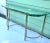 A 1960s Hollywood Regency demi-lune console table with a brass-tone metal frame and substantial beveled glass top. Its...