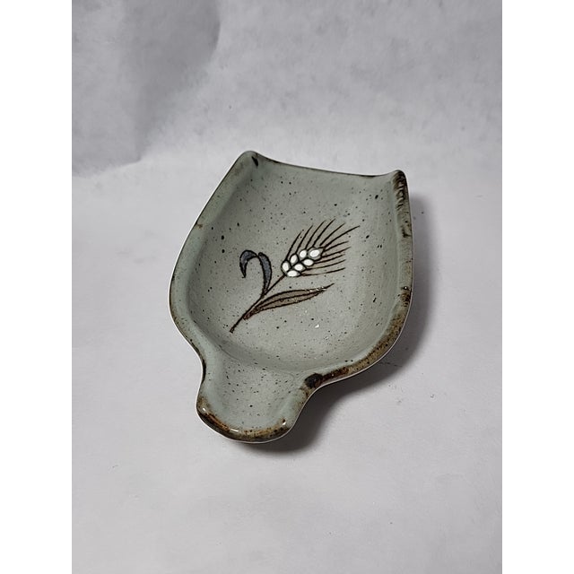 A gray and brown speckled studio pottery glazed spoon rest with handle. It is accented with shades of blue, and brown.