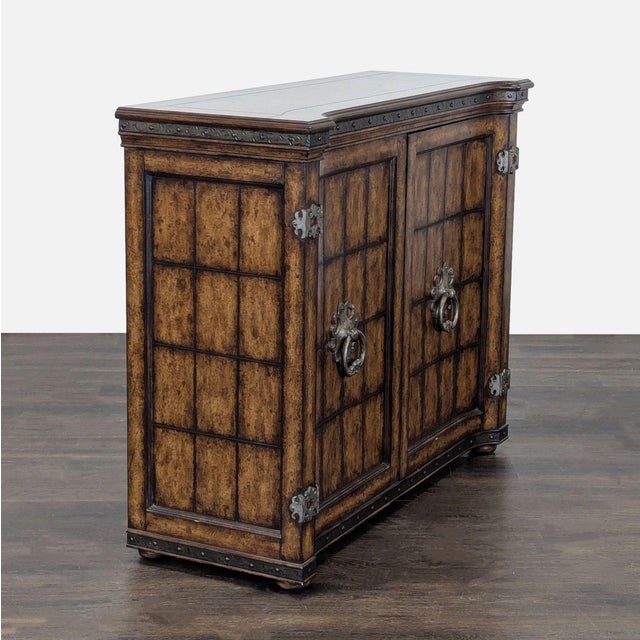 This cabinet features a rich wood finish with detailed metal accents and decorative handles. It has two front doors that...