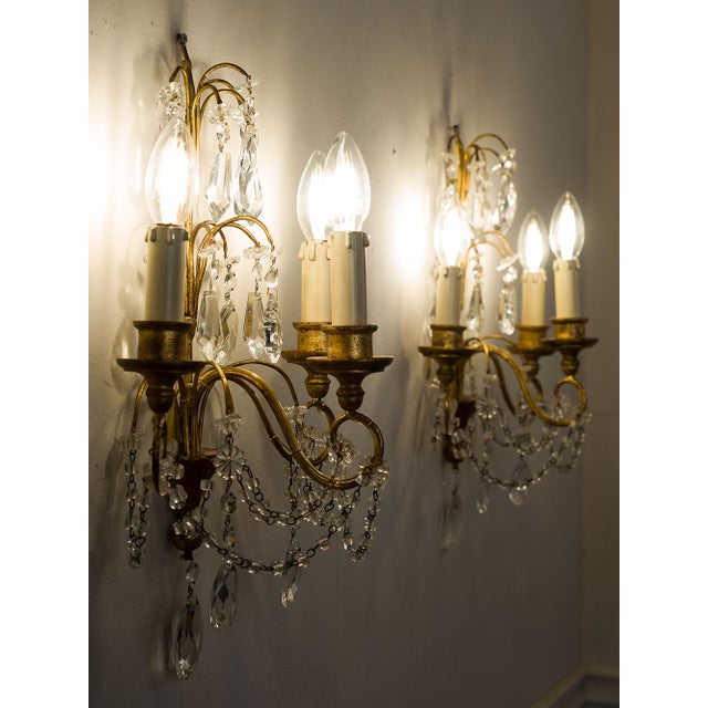 A pair of Florentine sconces in iron, gilded wood, and crystal, crafted in the mid-20th century. The three-light structure...