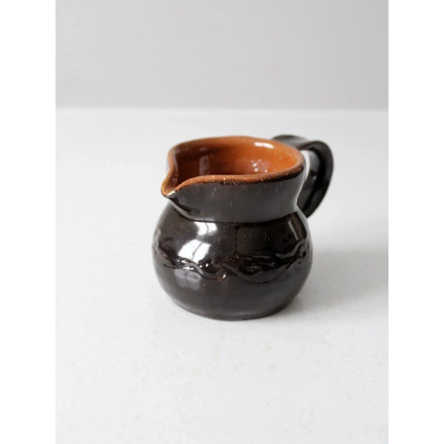 A vintage studio pottery creamer pitcher, hand-crafted and signed by the artist. The sculptural form features a rich dark...