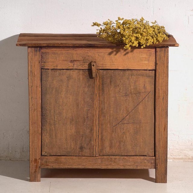 This antique low cupboard in pine wood is a Central European peasant cabinet with two doors and a wooden turn-latch. It...