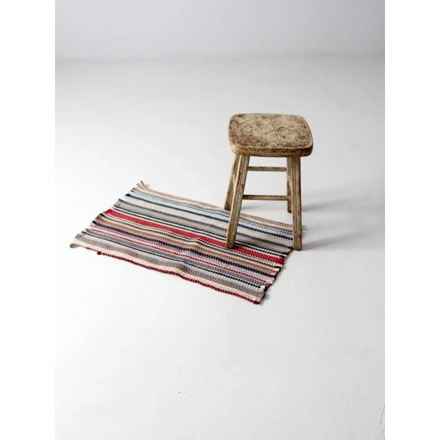 Vintage accent rug featuring a striped pattern in muted brick red, black, navy, gray, and white. This small throw rug...