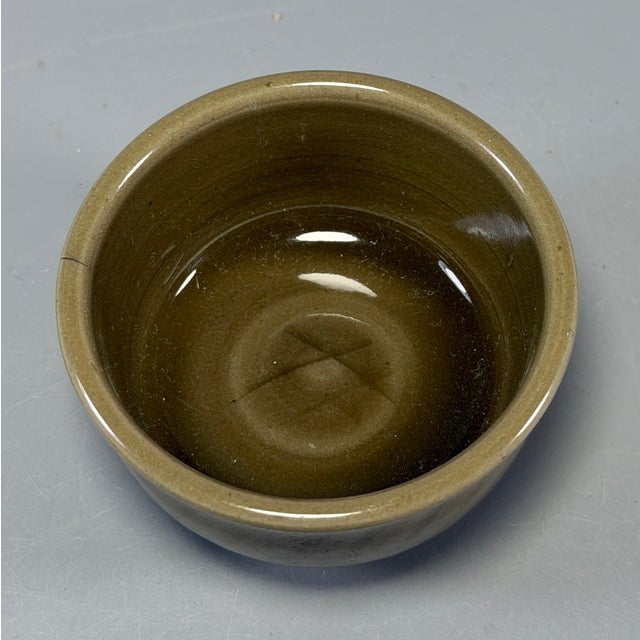 This vintage‑style celadon tea bowl is covered with glossy dark‑toned glaze. Its outer wall is decorated with neat slanted...