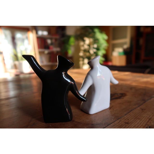 A pair of modern ceramic salt and pepper shakers designed as stylized human figures, executed in contrasting black and...