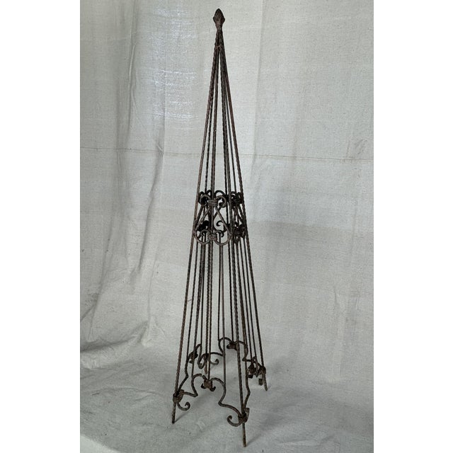 A hand forged wrought iron garden obelisk or trellis. Crafted with twisted iron uprights, decorative scrollwork, and...