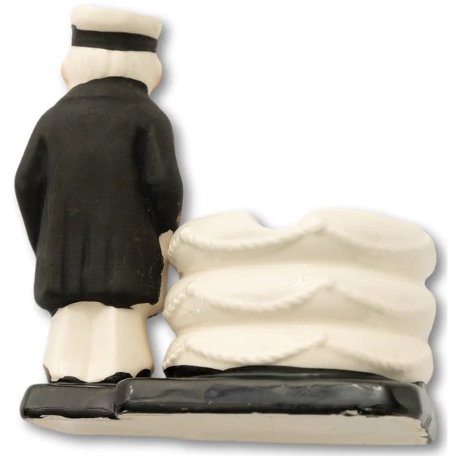Sz: 4 1/2"H x 4"W x 3"D Matte-coated sea captain standing next to a nest/ stack of life rings, suitable for use as an...