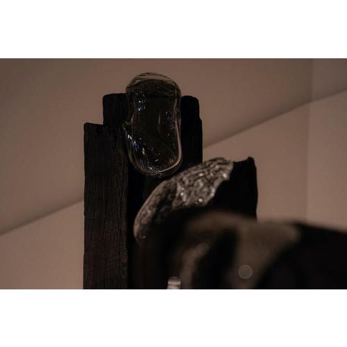 A sculptural group of three totems made of charred acacia wood, blown glass, and zinc bases. Each piece features carved...