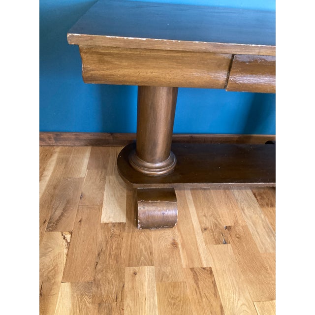 A striking vintage Art Deco console table featuring thick cylindrical legs and classic scroll feet. The center drawer is...