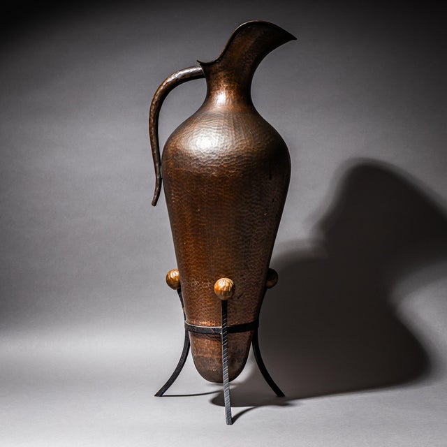 Decorative large vessel in hammered copper with a long handle and conical body. The tripod base is made of iron and...