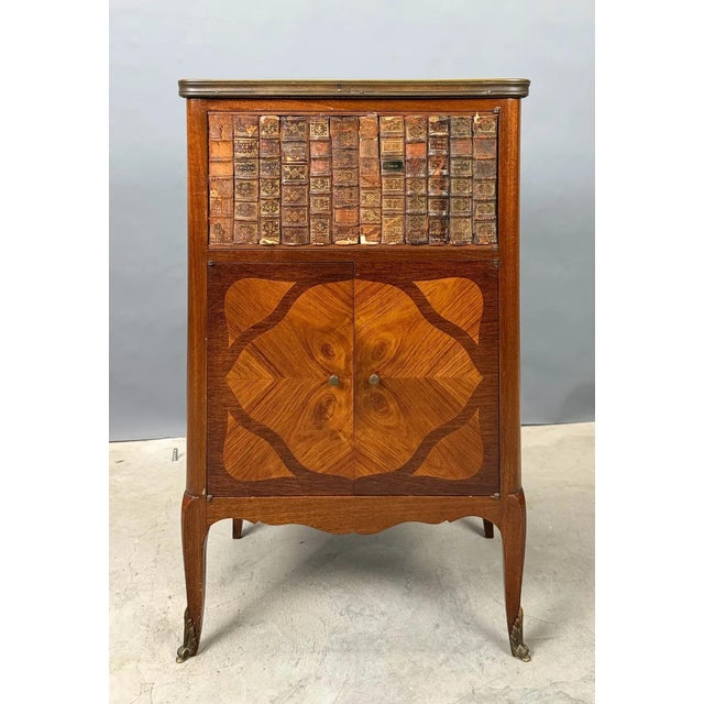 French Louis XVI-style faux-book cabinet with marble top, decorative veneers, marquetry and gilt-metal accents....