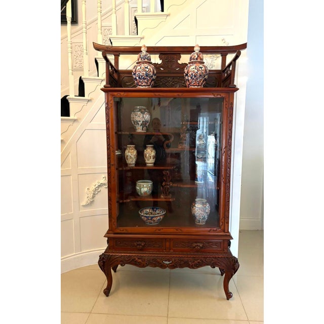 A striking antique Japanese display cabinet crafted in richly toned hardwood and finished in a deep red lacquer. The...