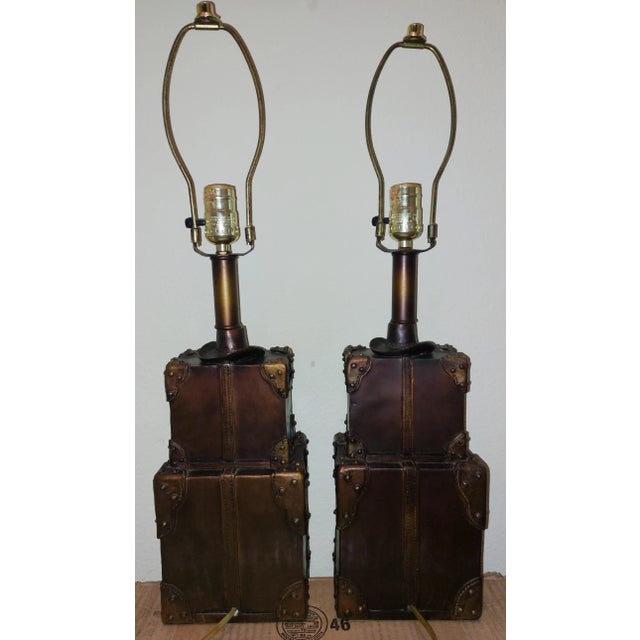 This listing is for TWO circa 1980s unbranded metal table lamps, styled to look like stacked old leather steamer/travel...
