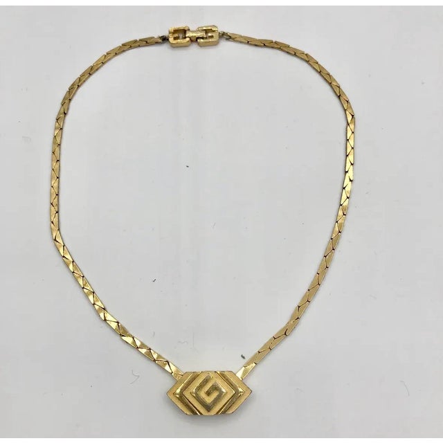 An elegant vintage Givenchy choker necklace featuring a sculptural, hexagonal G emblem suspended from a sleek gold-tone...